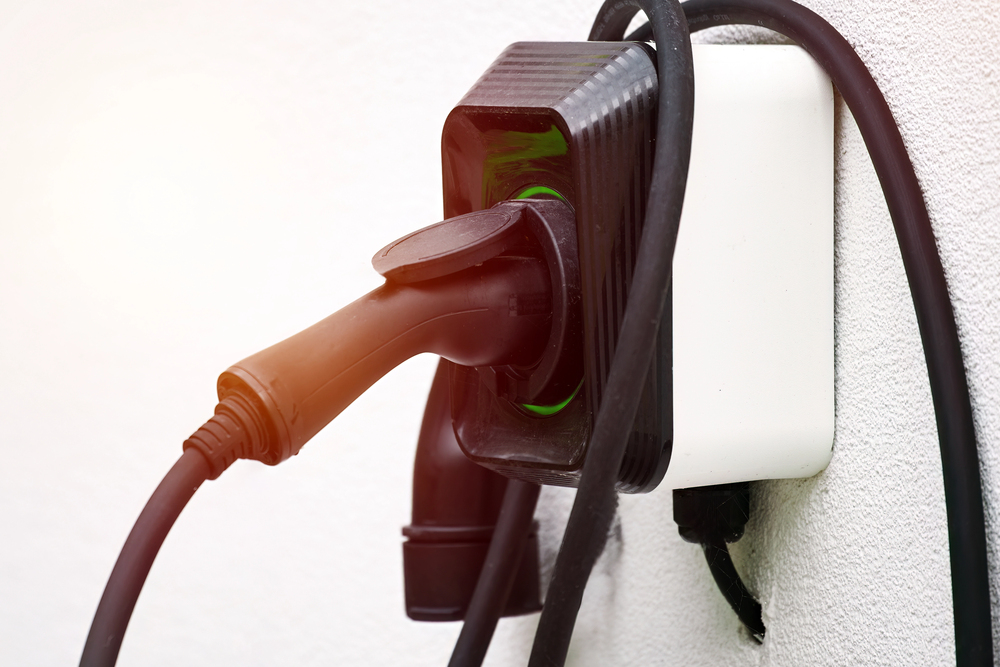 A close-up of an electric vehicle charging plug connected to a wall-mounted charging station.