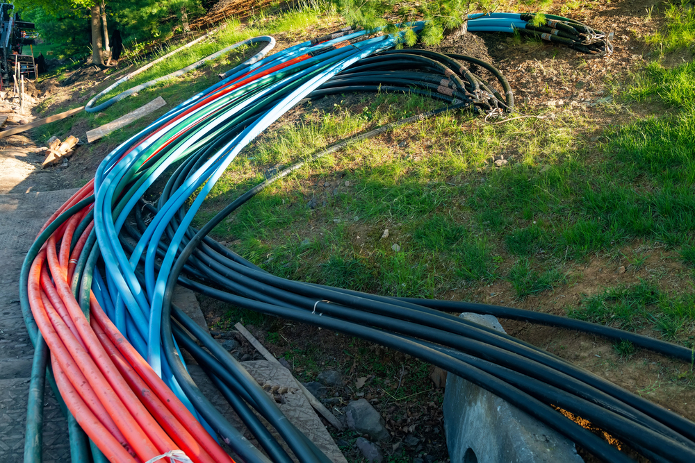 Several bundles of red, blue, and black cables are laid out on the ground near a grassy slope, with some coiled sections visible.