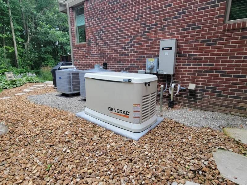 A standby Generac generator and an outdoor HVAC unit are installed next to a brick house, surrounded by gravel and landscaping stones.