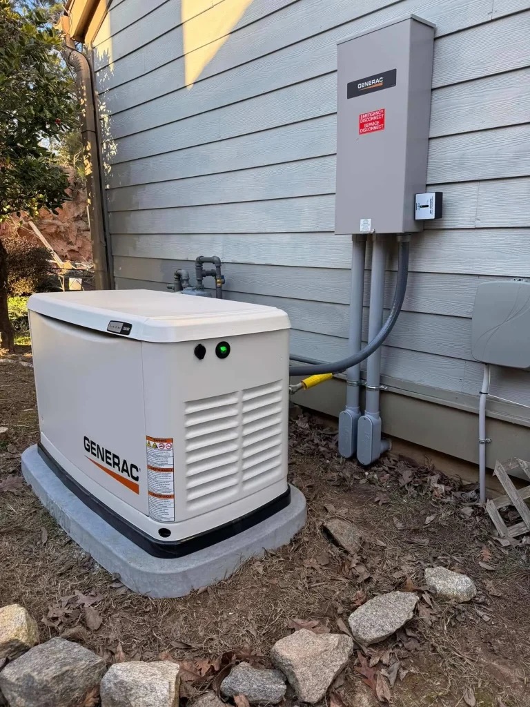 A Generac standby generator is installed on a concrete pad outside a house, connected to an electrical panel mounted on the exterior wall.
