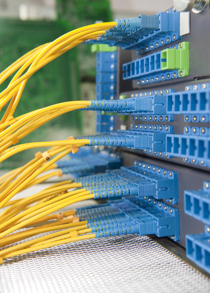 A close-up of yellow fiber optic cables connected to blue ports on a network server panel.